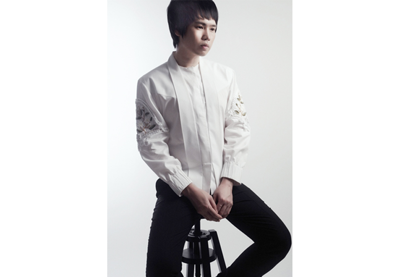 A man with stylish white attire and black pants is sitting on the stool